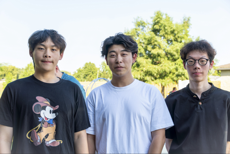 Three young men are standing side by side outdoors.