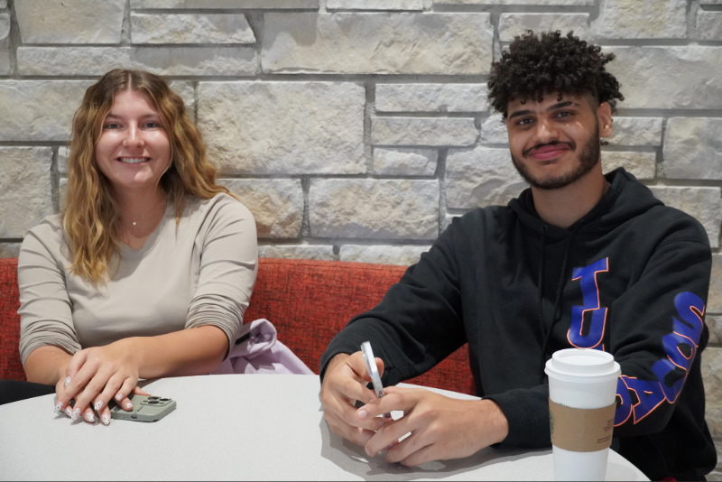 Two students sitting at a round table in front of a stone wall.