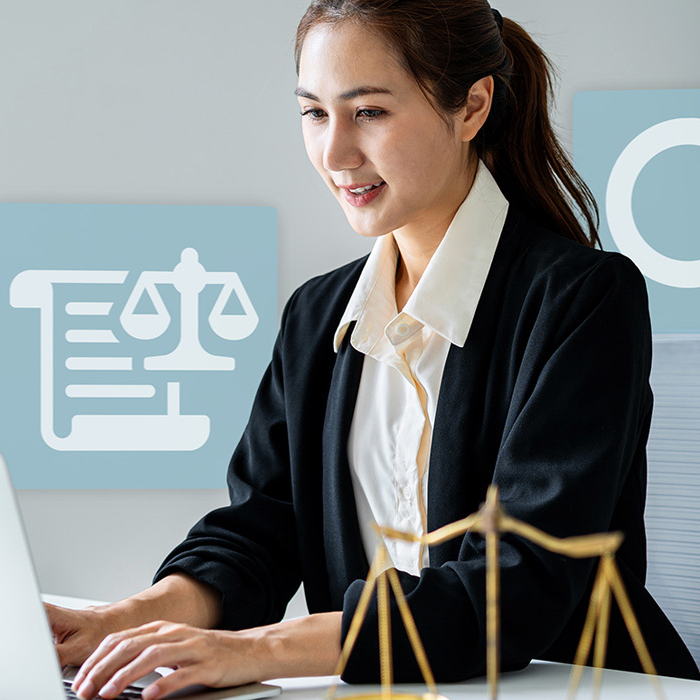 Smiling businesswoman in a black blazer types at a laptop beside blurred scales of justice.