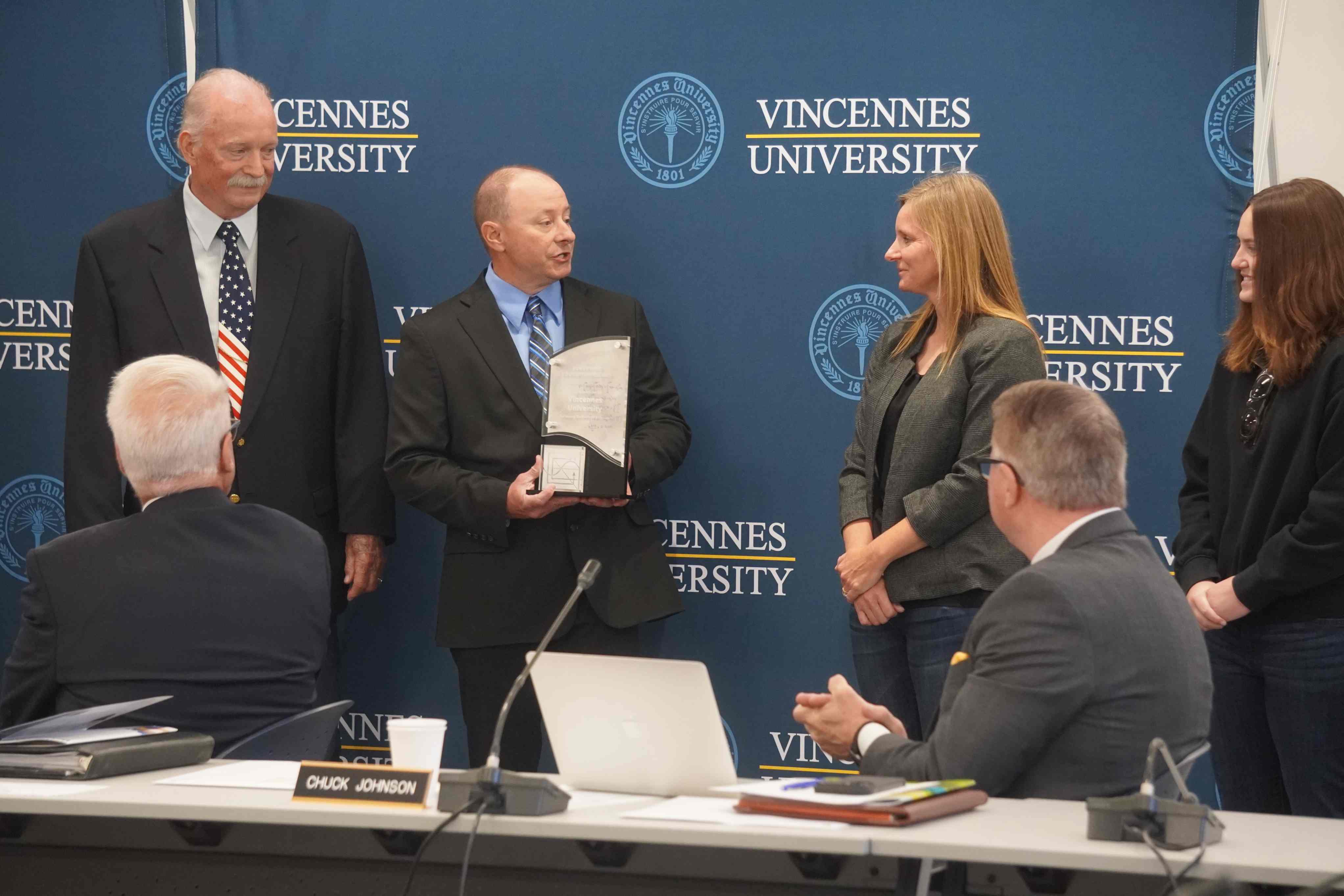 Jessica Hess smiles as a man presents her with an award plaque during a ceremony in front of a Vincennes University backdrop.   