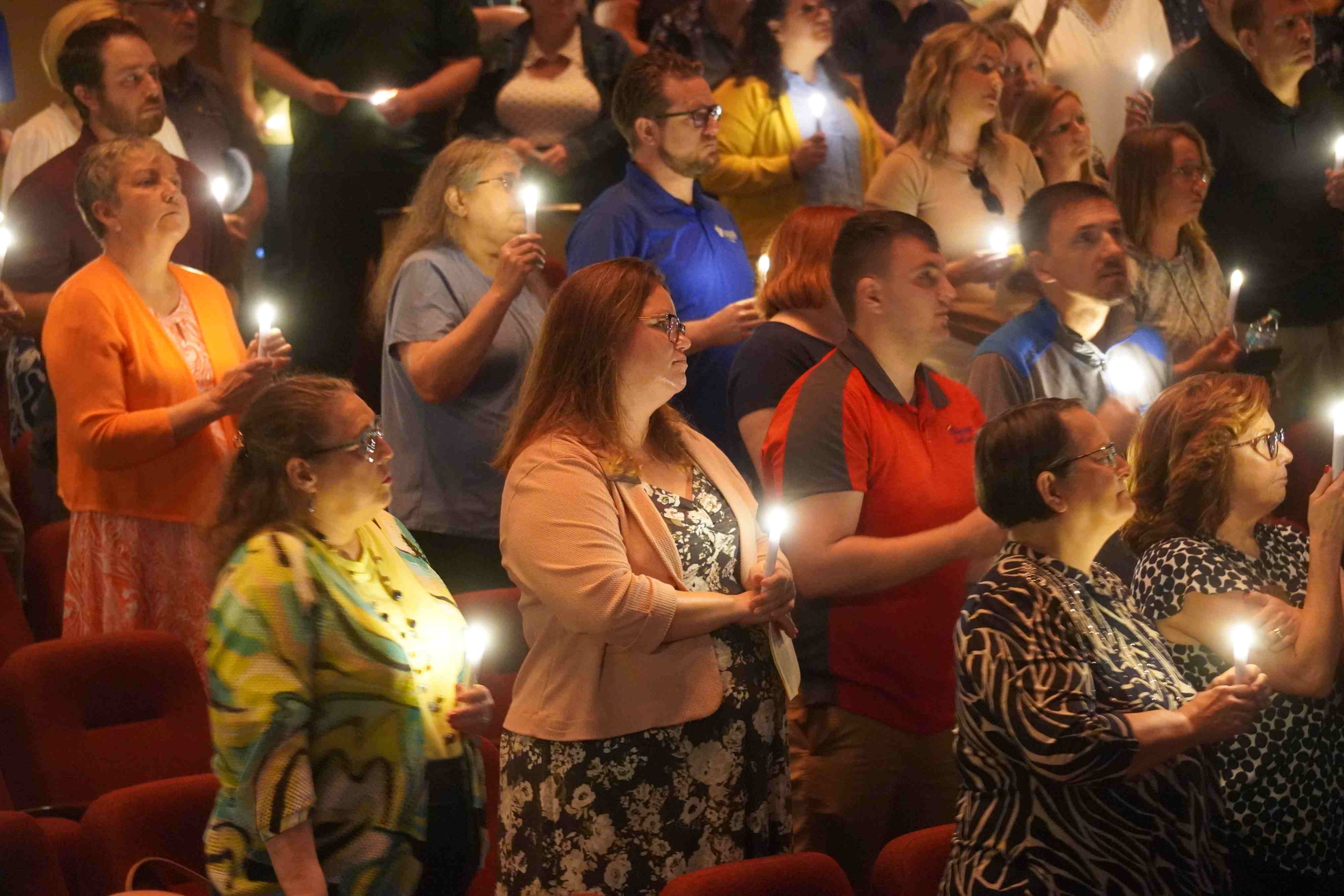 A group of VU faculty and staff standing in a dimly lit theater, holding small, glowing white candles during a light the torch ceremony.