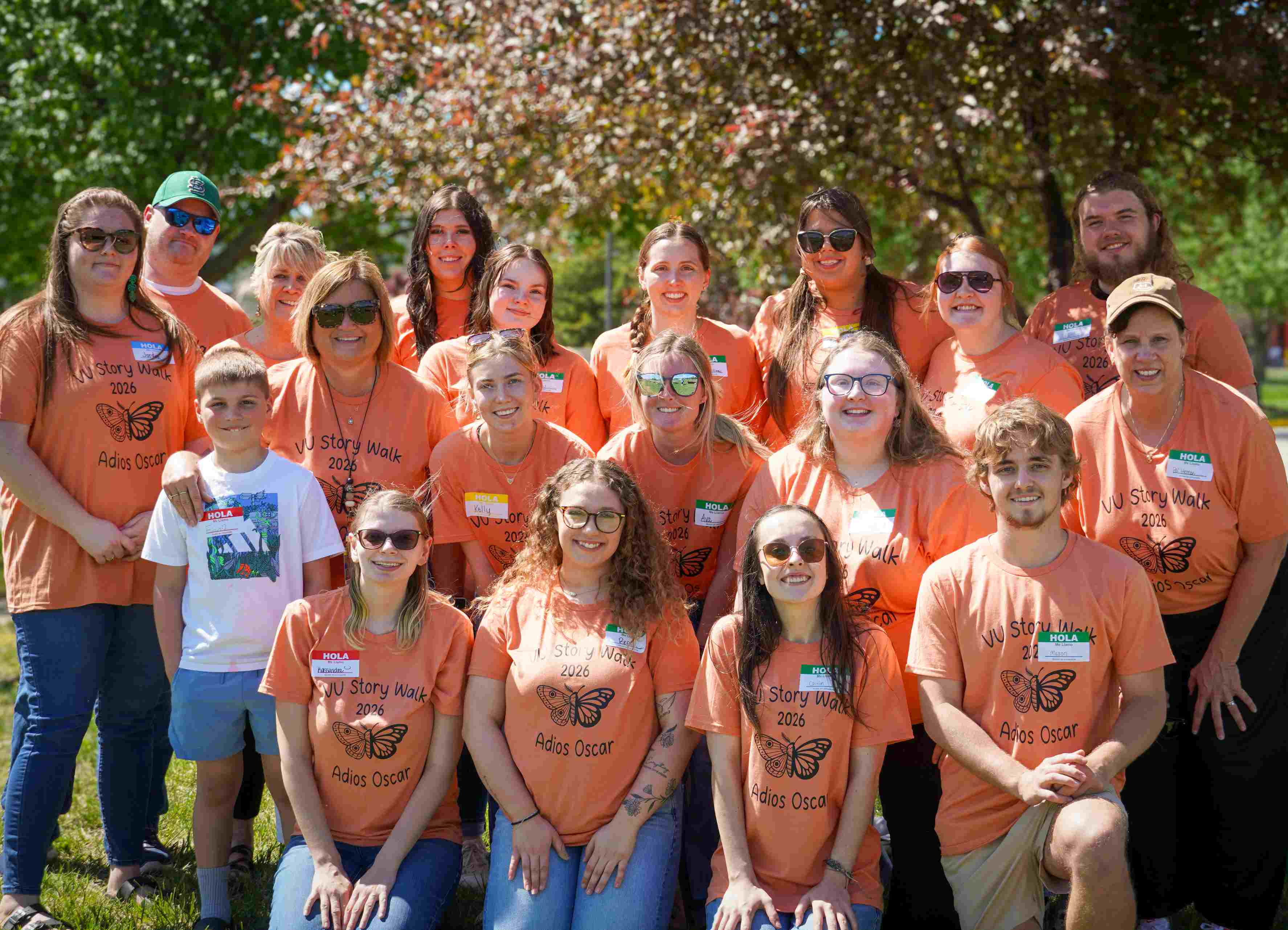 A large group of students and faculty outdoors smiling while wearing matching orange 