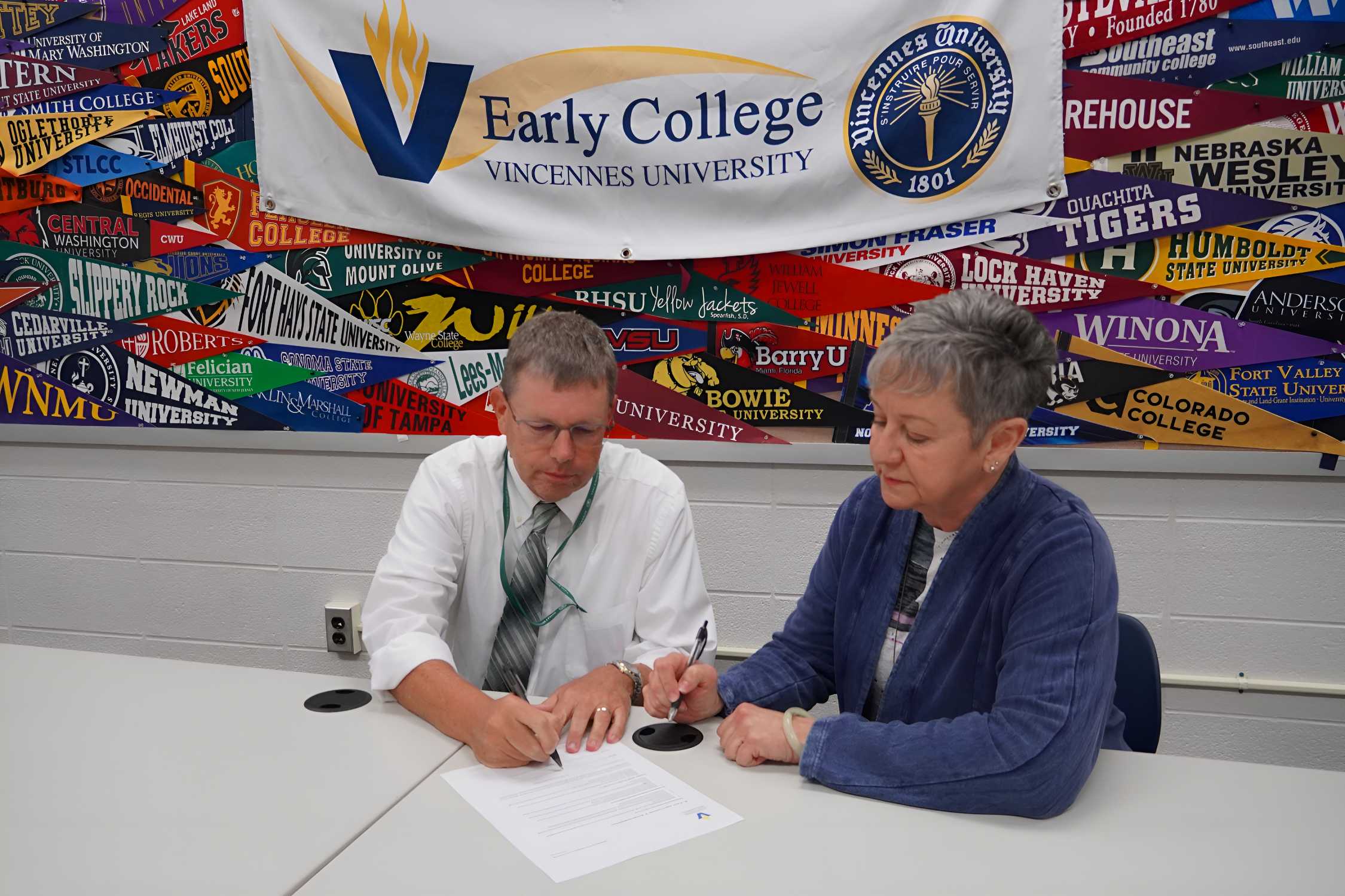 Greg Parsley and Cynthia Ragle sit at a table signing a document in front of a Vincennes University Early College banner.