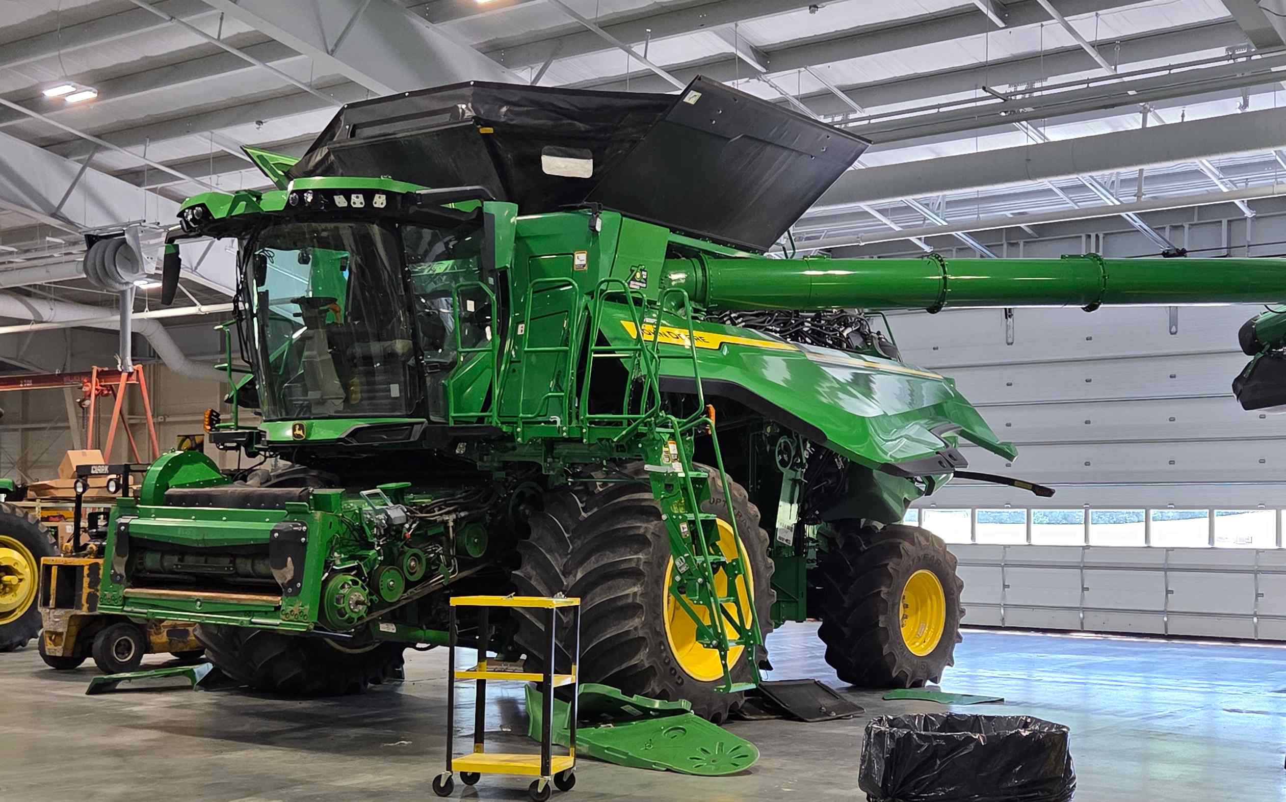 A large green and yellow John Deere combine harvester parked inside a spacious industrial lab at the Vincennes University Ag Center