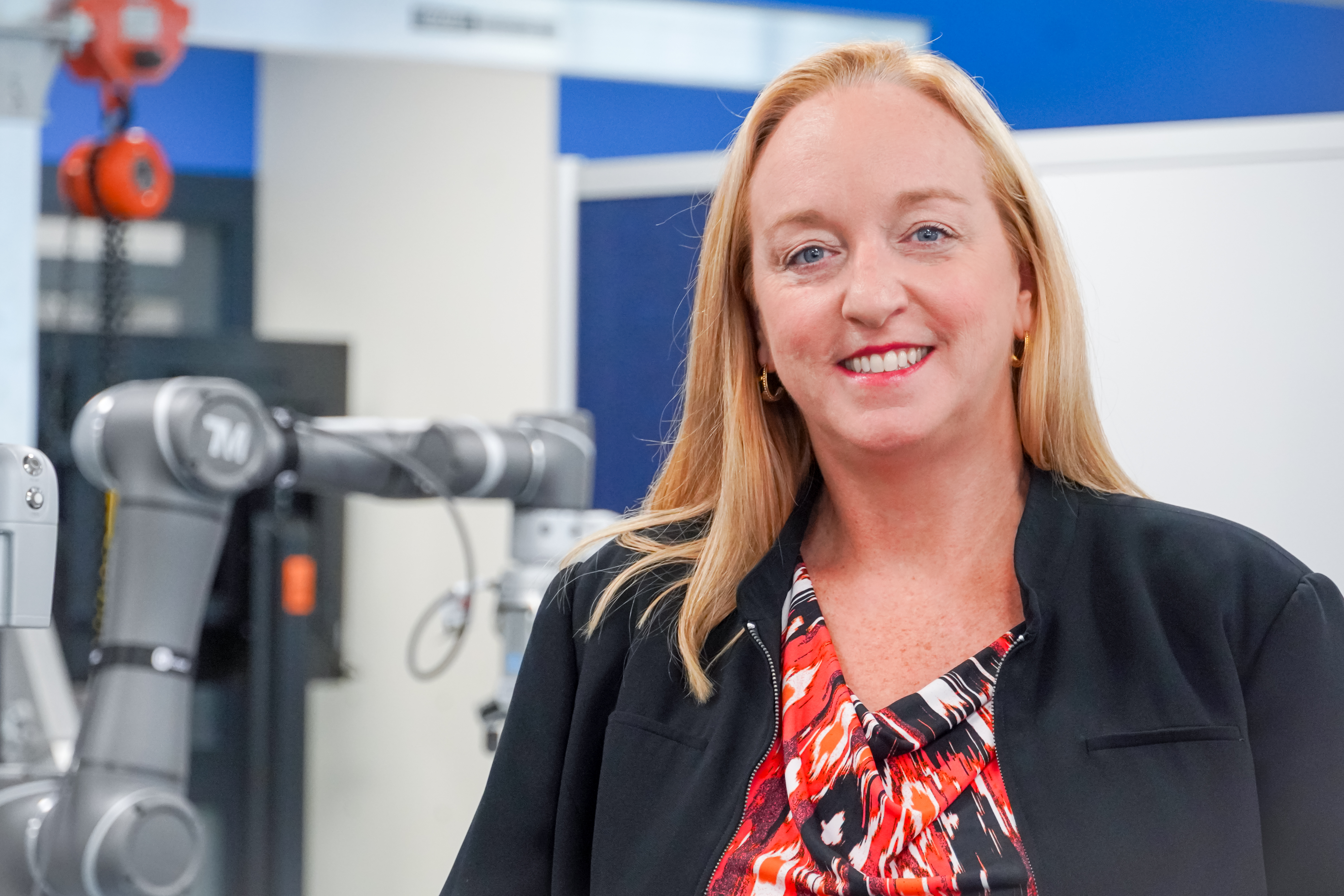 Kimberly Wright smiling in the CARA on the Vincennes University Campus. There is a cobot in the background of the photo.